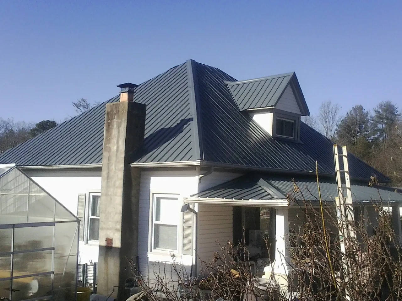 Dark blue standing seam metal roof on a white farmhouse with dormer — Slate & Tile Roof Repair by Roofing Brothers in Colliersville