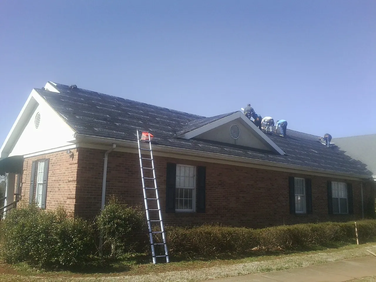 Crew tearing shingles off a brick ranch roof with a ladder set — Emergency Roof Repair work by our crew in Colliersville