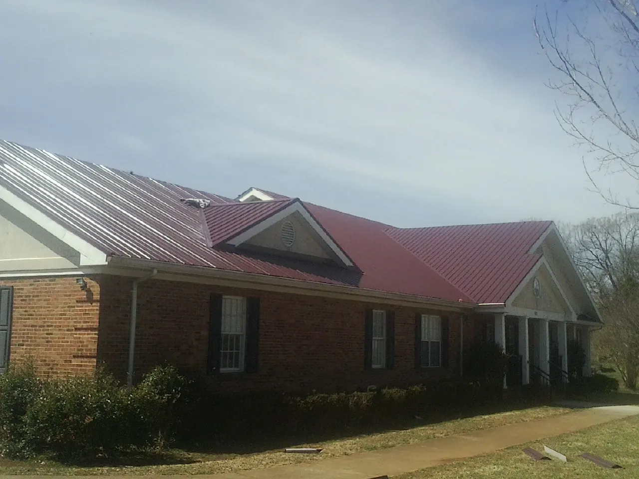 Red metal roof with gabled entries on a long brick building, from a Hail Damage Roof Repair job in Colliersville