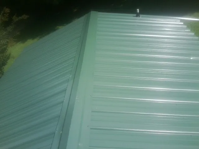 New green metal panels meeting at the ridge of a roof — Flat Roof Repair work by our crew in Colliersville