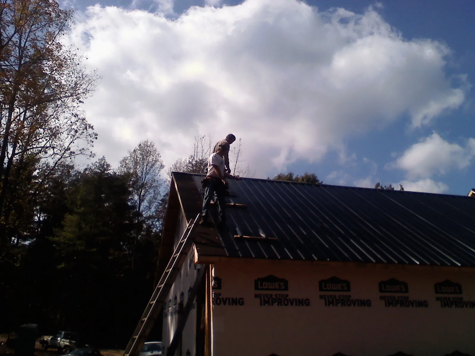 Roofer fastening dark metal panels high against a cloudy sky, from a Roof Inspection job in Colliersville