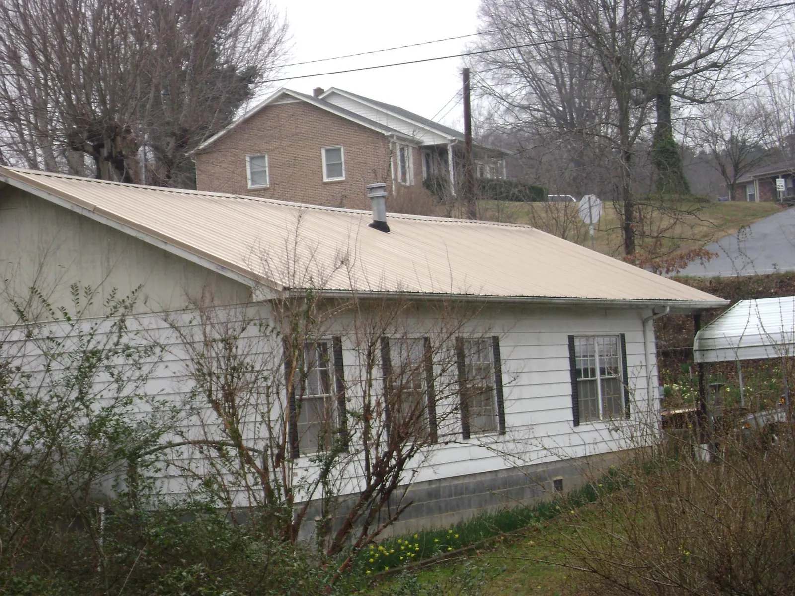 Tan metal roof on a white sided house set into a hillside — Commercial Roofing by Roofing Brothers in Colliersville